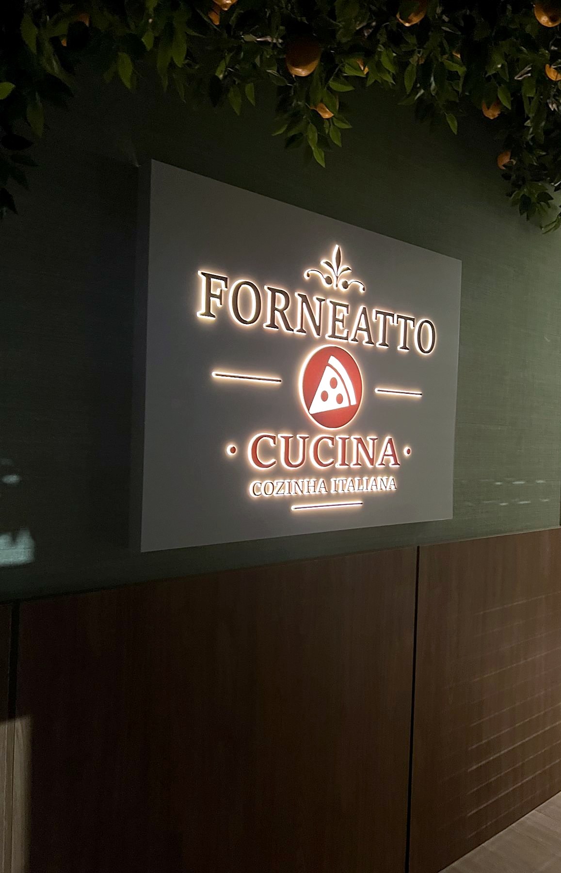 A fachada do Forneatto Cucina, Cozinha Italiana, com o letreiro aceso sob os limoeiros
